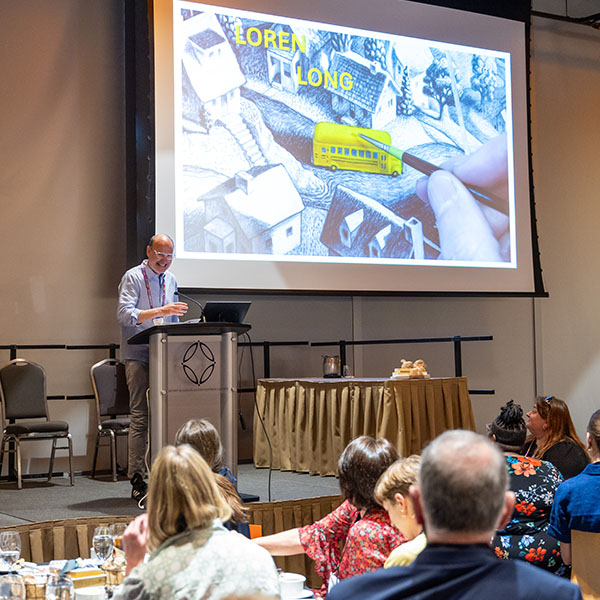 Author Loren Long at 2024 TLA Annual Conference Opening Awards and Author Luncheon reading from the podium.