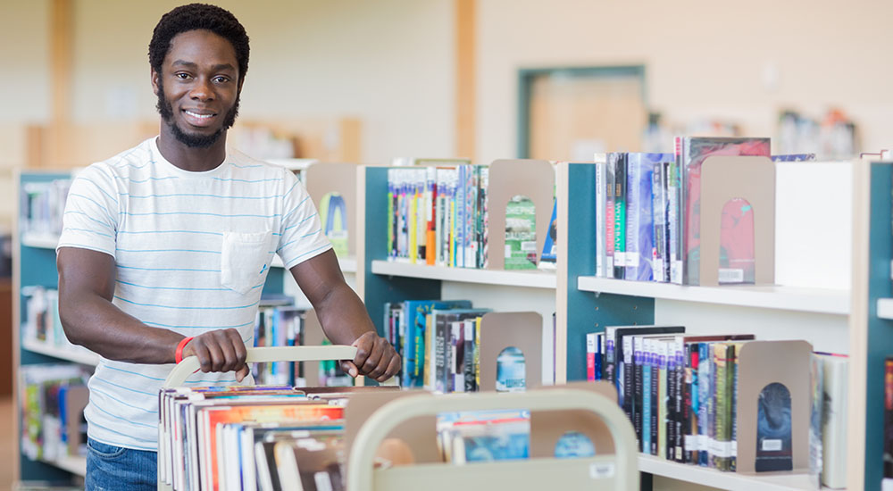 A male librarian pushing a book cart.