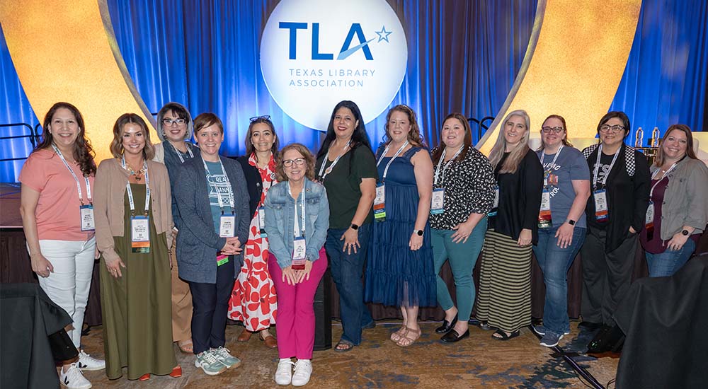 Group of TLA Annual Conference Attendees in front of a stage with TLA logo behind them