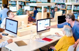 Library patrons sitting at a computer being helped by a librarian