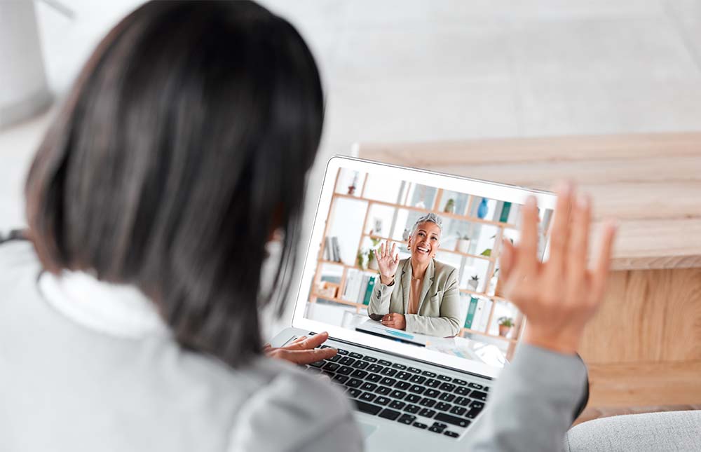 Woman on laptop waving to another woman onscreen