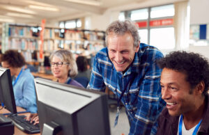 People at computer in library, a male librarian helping a male patron with two women on computers next to them