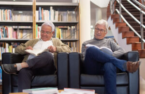 Two older men reading at the library sitting in chairs