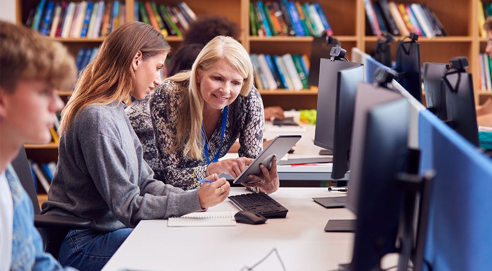 Librarian helping a student sitting at a row of computers with a male student