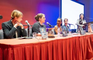 Four authors sitting at a table speaking with a moderator at a podium at the TLA Annual Conference.