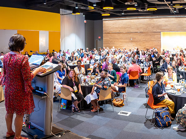 Speaker at a podium on a raised stage looking out to the audience of TLA Annual Conference Attendees