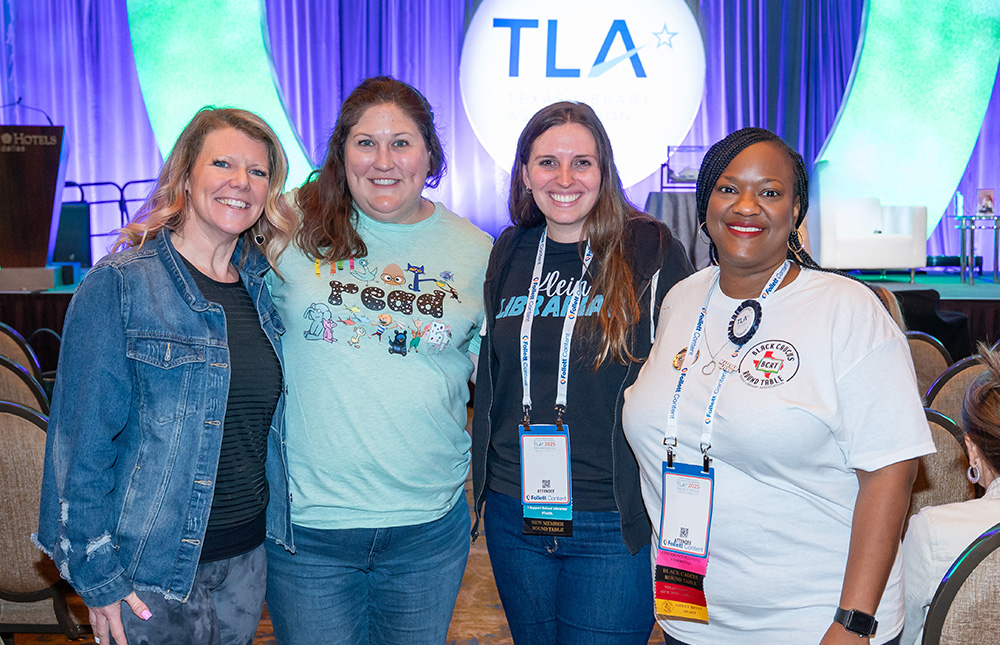 Four women stand in front of stage with TLA logo sign